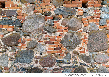 A rustic stone wall features various shapes and tones of natural stones arranged harmoniously. 126326667