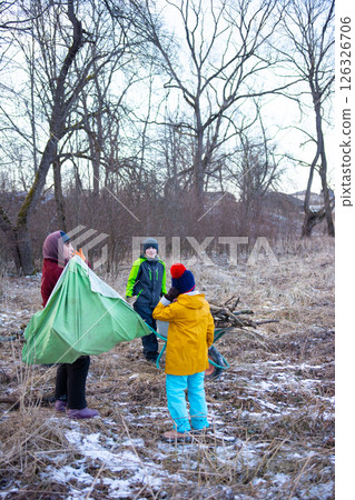 Gathering in nature while children assist with setting up a camping experience in the wilderness during the late afternoon chill of early spring Gathering in nature while children assist with setting up a camping experience in the wilderness during the late afternoon chill of early spring 126326706