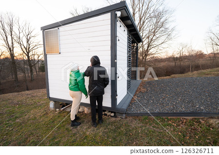 Exploring a modern storage structure near a peaceful landscape at dusk while two people enjoy the tranquility of nature 126326711
