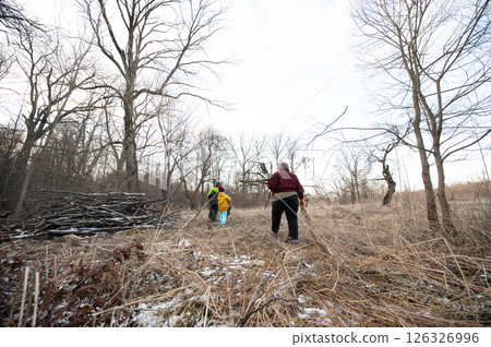 Exploring a Winter Landscape with Friends in the Early Afternoon Sunlight amidst Tall Grasses and Leafless Trees 126326996