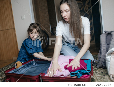 Tired mother with 6 year old daughter packing travel suitcase. Travel concept. Close-up of travel bag and tired faces of travelers. 126327742