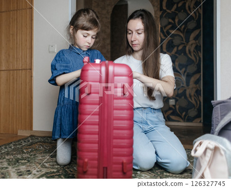 Tired mother with 6 year old daughter packing travel suitcase. Travel concept. Close-up of travel bag and tired faces of travelers. 126327745