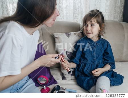 Mother putting makeup on her daughter face and they fool around together. Communication between women in the family. Fun time. Happy family concept. little girl doing her makeup 126327777