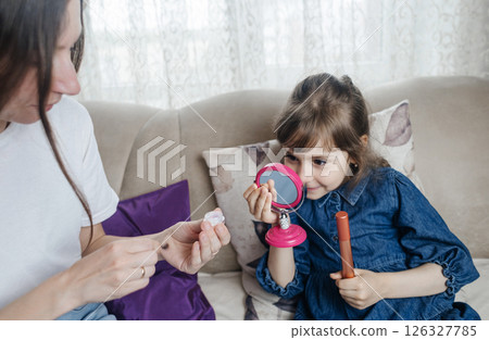 Mother putting makeup on her daughter face and they fool around together. Communication between women in the family. Fun time. Happy family concept. little girl doing her makeup Mother putting makeup on her daughter face and they fool around together. Communication between women in the family. Fun time. Happy family concept. little girl doing her makeup 126327785