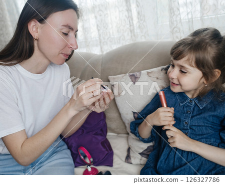 Mother putting makeup on her daughter face and they fool around together. Communication between women in the family. Fun time. Happy family concept. little girl doing her makeup 126327786