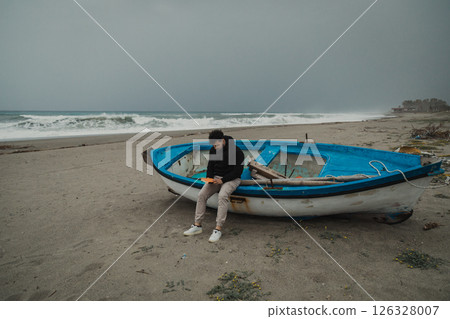 Man Reading A Book Sitting On The Beach In Winter Near A Boat Man Reading A Book Sitting On The Beach In Winter Near A Boat 126328007