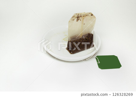 used tea bag with a long thread and paper green lable, on a small white saucer with tea stains 126328269