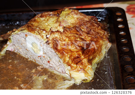 meat roll with eggs in Savoy cabbage leaves. last half, on baking sheet, in its own juice. on cut, you can see half of a whole egg, surrounded by cooked, pleasant-colored, minced meat with spices 126328376