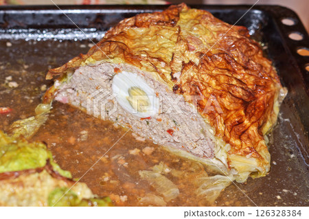 homemade meatloaf with eggs in Savoy cabbage leaves. last half, on baking sheet, in its own juice. on cut half of a whole egg, surrounded by baked, pleasant-colored, minced meat with spices homemade meatloaf with eggs in Savoy cabbage leaves. last half, on baking sheet, in its own juice. on cut half of a whole egg, surrounded by baked, pleasant-colored, minced meat with spices 126328384
