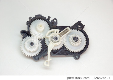 cogwheels mechanism in black plastic case. Part of inkjet printer: complex mechanical drive made of Multiple reducer gears of white plastic and spring 126328395
