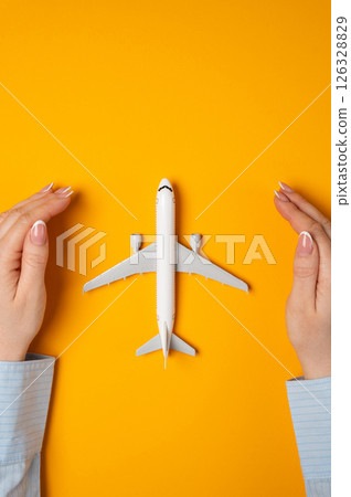 Hands protect a passenger plane on a yellow background. Air travel insurance, tourism risk coverage. Protection of the civil aviation industry. Airline regulation themes. Hands protect a passenger plane on a yellow background. Air travel insurance, tourism risk coverage. Protection of the civil aviation industry. Airline regulation themes. 126328829