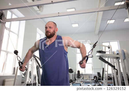Male athlete bodybuilder exercising in the gym. Strength training on a cable machine. 126329152