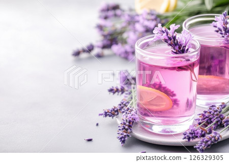 A refreshing and elegant beverage photography featuring lavender lemonade in clear glass tumblers garnished with fresh lavender sprigs and lemon slices.  126329305