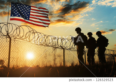 Silhouetted Figures of Soldiers Against Barbed Wire Fence with US Flag Background Depicting National Border Security. memorial day concept Silhouetted Figures of Soldiers Against Barbed Wire Fence with US Flag Background Depicting National Border Security. memorial day concept 126329523
