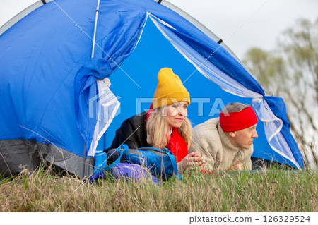 Active elderly Caucasian couple relaxing in a tent against the backdrop of autumn natural landscape. Man and woman tourists on a trip. Active elderly Caucasian couple relaxing in a tent against the backdrop of autumn natural landscape. Man and woman tourists on a trip. 126329524