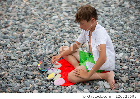 The child paints on sea stones. He is creative during the holidays. The child paints on sea stones. He is creative during the holidays. 126329593