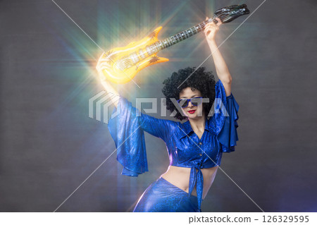 Girl comic pop star posing in black wig with toy guitar on blue background. Rock style of seventies 126329595