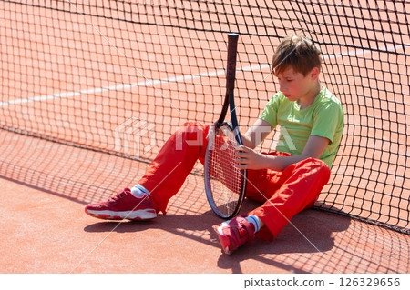 The boy lost the tennis competition. The child sits at the net with a racket. Psychology of sports in childhood. The boy lost the tennis competition. The child sits at the net with a racket. Psychology of sports in childhood. 126329656