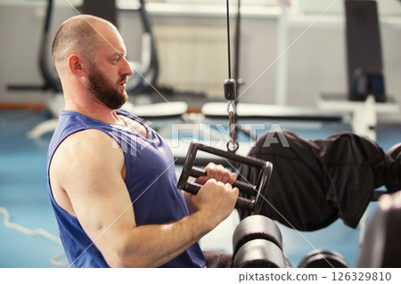A male athlete is working out in a gym. He is bald and has a beard. 126329810