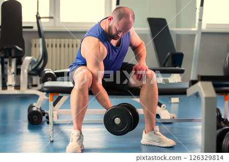 A man lifts weights in a gym. He holds a dumbbell in one hand. 126329814