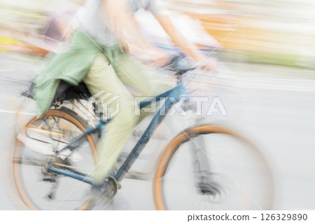Woman riding bicycle in light green pants with jacket tied at waist, captured in motion blur. Healthy lifestyle, leisure activity concept. Concept of casual city cycling, ecology, green transport 126329890