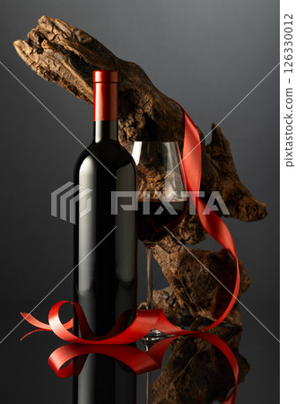 Bottle and glass of red wine on a black reflective background. 126330012
