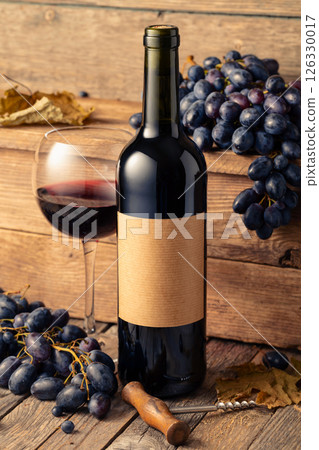 Bottle of red wine and blue grapes on a old wooden table. 126330017