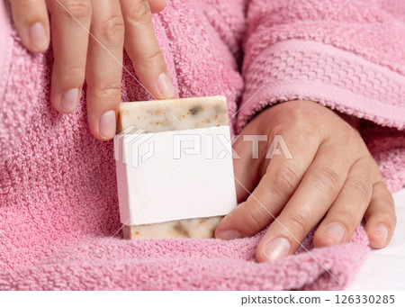 Closeup of woman in pink bathrobe holding soap bar with blank label in hands, mockup Closeup of woman in pink bathrobe holding soap bar with blank label in hands, mockup 126330285