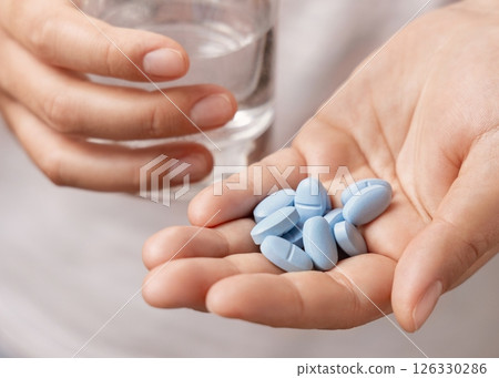 Woman in white t-shirt holding blue pills in cupped hand and water glass in hand closeup 126330286
