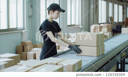 Female postal worker sorting packages on conveyor belt in distribution warehouse 126330304