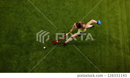 Hockey player drives forward in full stride on green grass field against white studio background, symbolizing control and power. Hockey player drives forward in full stride on green grass field against white studio background, symbolizing control and power. 126331143