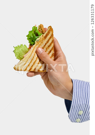 Hand holding grilled triangle sandwich with toasted bread, lettuce, ham, herbs, and sauce against clean white background. Hand holding grilled triangle sandwich with toasted bread, lettuce, ham, herbs, and sauce against clean white background. 126331179