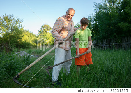 A man and a boy, father and son, work together in the field. They mow the grass. The scene represents collaboration and teamwork. 126331215