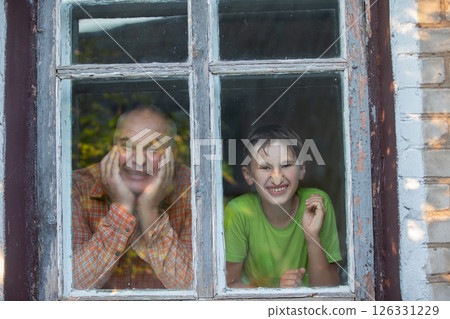 Grandfather and grandson look out of the window of a village house and grimace. Father's Day. 126331229
