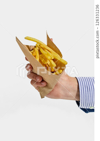 Hand holding paper cone filled with golden crispy French fries, ready to snack on street-style favorite comfort food against white background. Hand holding paper cone filled with golden crispy French fries, ready to snack on street-style favorite comfort food against white background. 126331236