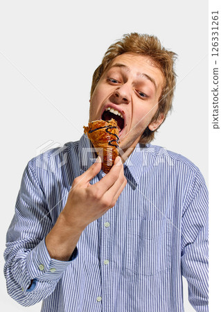Man in striped shirt holding croissant and tilting head back with open mouth ready for big bite with playful expression against white studio background. Man in striped shirt holding croissant and tilting head back with open mouth ready for big bite with playful expression against white studio background. 126331261