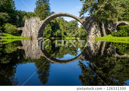 a semi-circular arched bridge made of basalt over a pond reflected in the water 126331300