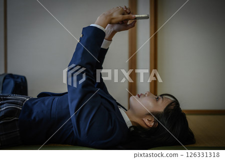 High school girl lying down in a Japanese-style room and looking at her smartphone: Bullying, school refusal, SNS troubles, social issues High school girl lying down in a Japanese-style room and looking at her smartphone: Bullying, school refusal, SNS troubles, social issues 126331318