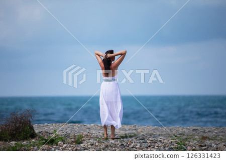 A full-length woman in a white dress looks at the sea. A full-length woman in a white dress looks at the sea. 126331423