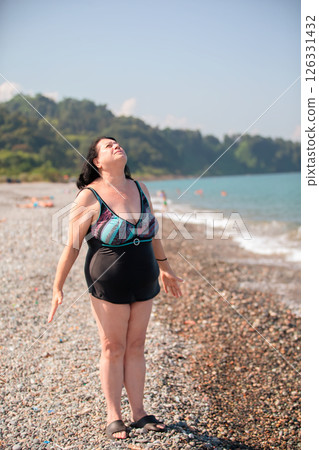 An elderly woman in a swimsuit does sports and breathing exercises on the beach. An elderly woman in a swimsuit does sports and breathing exercises on the beach. 126331432
