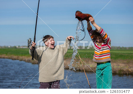 Funny fishing. Two of the boy's friends hooked an old shoe with a fishing rod and are laughing. Funny fishing. Two of the boy's friends hooked an old shoe with a fishing rod and are laughing. 126331477