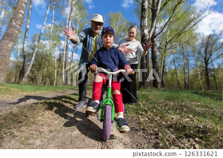 A grandson with his grandparents riding a bike in the park. 126331621