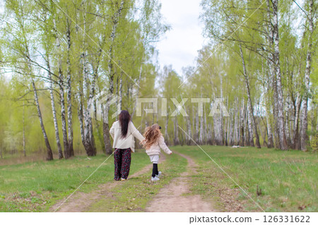 Mom and daughter are walking through a birch grove with their backs to the camera. 126331622