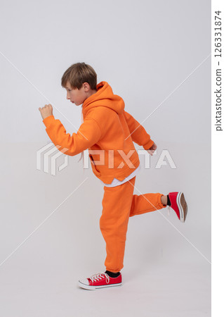 A teenage boy in an orange jumpsuit and red shoes. He pretends to run with his arms outstretched. 126331874