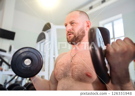A male athlete lifts weights in the gym. He is bald and has a beard. A male athlete lifts weights in the gym. He is bald and has a beard. 126331948