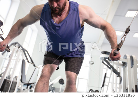 Male athlete bodybuilder exercising in the gym. Strength training on a cable machine. 126331950