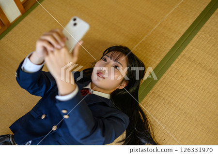 A high school girl lying down in a Japanese-style room and looking at her smartphone: Contact, career advice, SNS, game app, in-app purchases 126331970