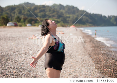 An elderly woman in a swimsuit does sports and breathing exercises on the beach. An elderly woman in a swimsuit does sports and breathing exercises on the beach. 126331999