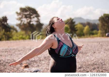 An elderly woman in a swimsuit does sports and breathing exercises on the beach. An elderly woman in a swimsuit does sports and breathing exercises on the beach. 126332000