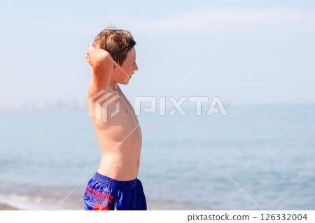 A teenage boy on the beach put his hands behind his head and admires the sea. 126332004